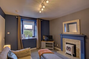 Ein Zimmer mit Fernseher, Kamin, einem fenster mit Vorhängen und einer Couch.