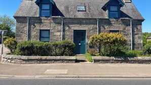 A stone house with a green door, two chimneys, and a small window. - A 2-bedroom cosy cottage based at the heart of the rural village of Brora. (Brora)