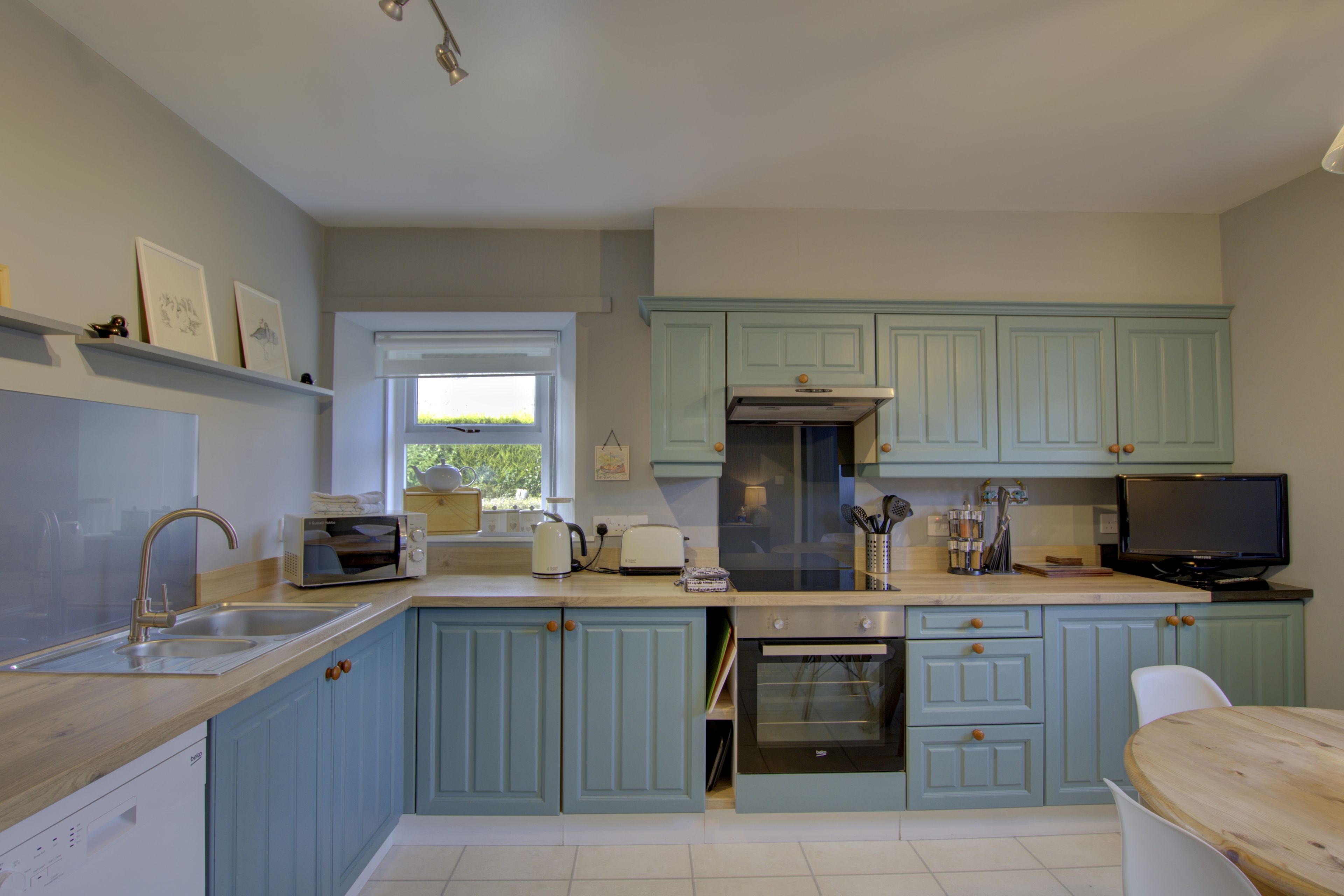 A kitchen with light blue cabinets, a built-in oven, a microwave, and a sink.