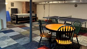 A room with a ping pong table, chairs, a table, and a carpet with a geometric pattern.