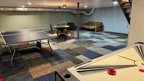 A ping pong table, chairs, a sofa, and a dartboard in a room with a checkered carpet and exposed ductwork.