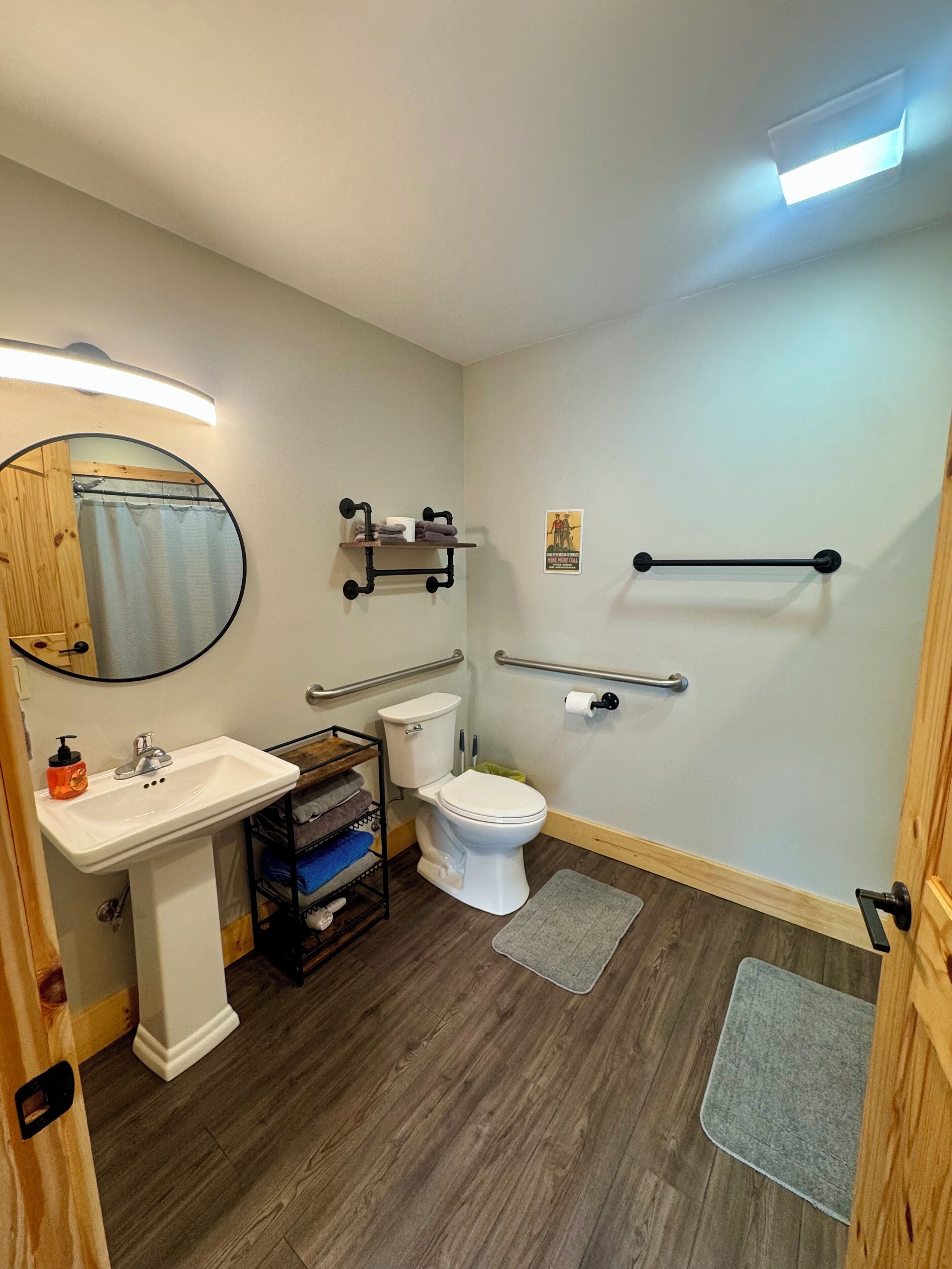 A bathroom with a white sink, toilet, and mirror, wooden floor, and a shower curtain.
