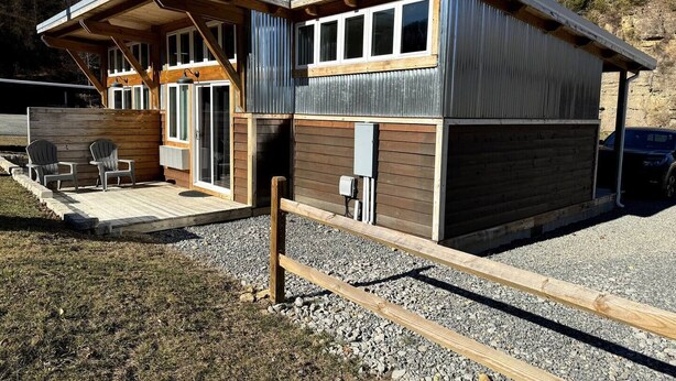 Eine moderne Hütte mit einer Terrasse, zwei Fenstern und einer Tür.