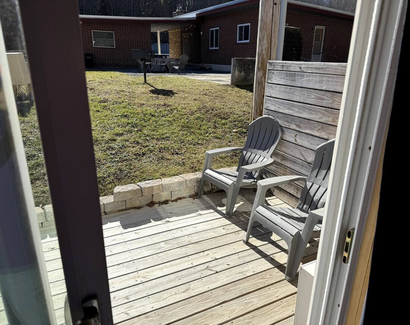 A wooden deck with Adirondack chairs, a brick house in the background, and a clear sky.
