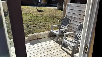 A wooden deck with Adirondack chairs, a brick house in the background, and a clear sky.