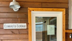 A wooden cottage entrance with a sign reading 'Conrad's Cottage,' a glass door, and a welcome sign for a trail camp.