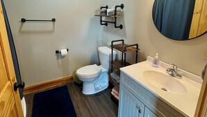 Un baño con inodoro, lavabo, espejo, toallero y puerta de madera.