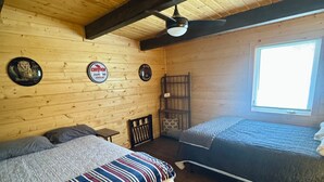 Una habitación tipo cabaña de madera con dos camas, un ventilador de techo y una ventana.