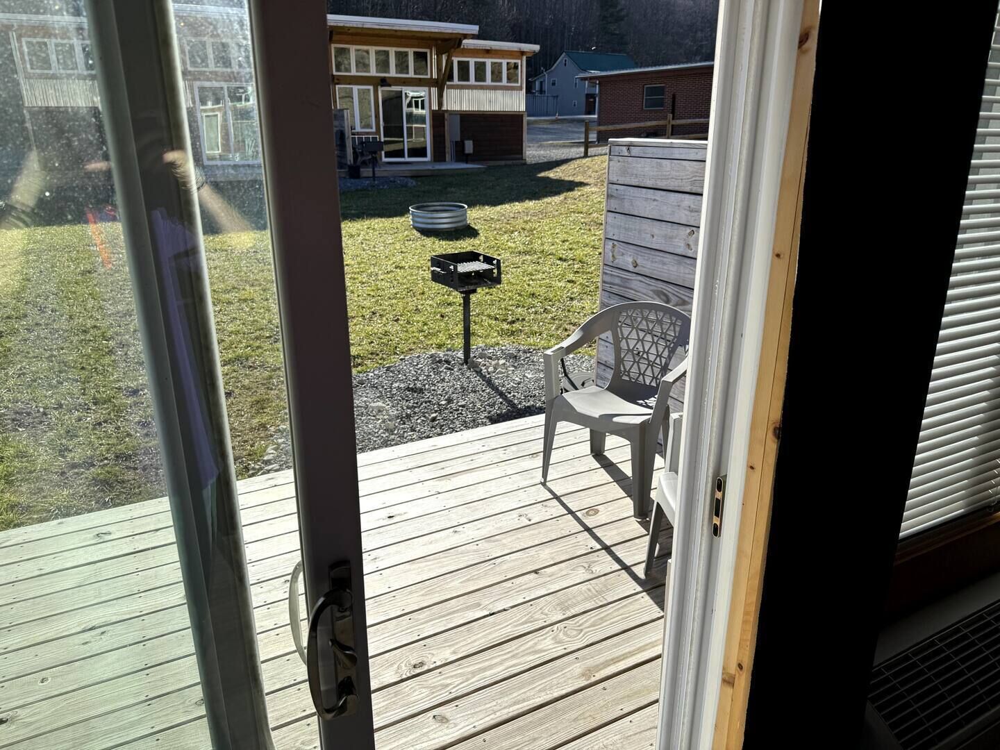 A wooden deck with a chair and a grill, overlooking a backyard with a house and a fenced area.