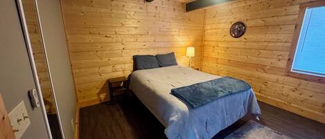 Een slaapkamer met houten lambrisering, een bed, een bedlamp en een raam.