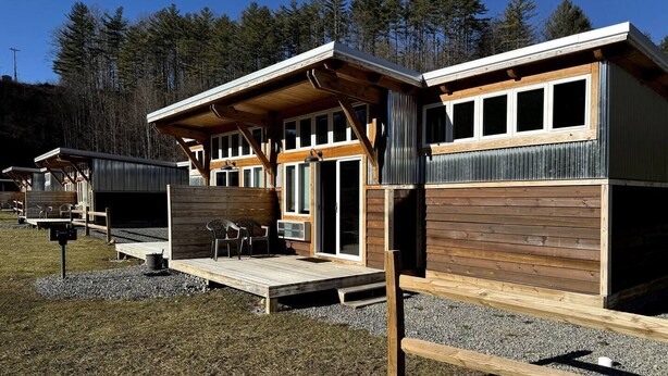 A row of cabins with wooden exteriors and large windows, set in a forested area.
