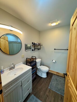 A bathroom with a white sink, wooden vanity, a toilet, a towel rack, and a mirror.