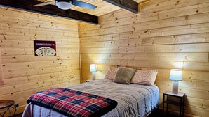 Un dormitorio con paneles de madera, una cama, dos lámparas de noche, un ventilador de techo y un cartel en la pared.