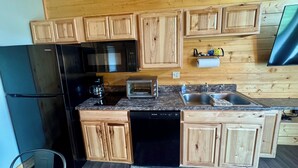 Una cocina con armarios de madera, un refrigerador negro, un microondas, un tostador y un lavavajillas.