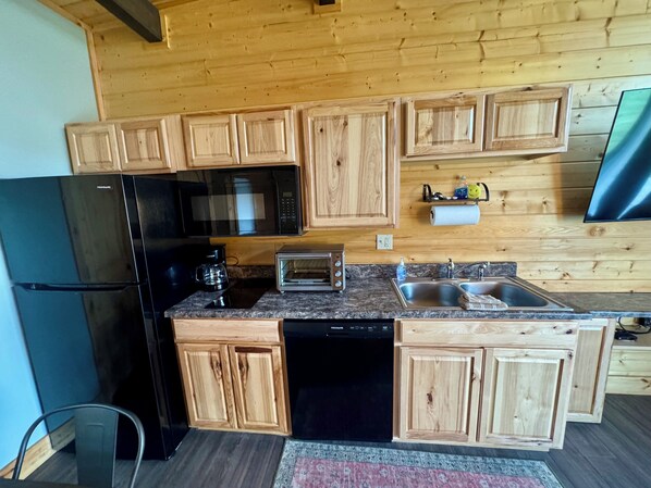 A kitchen with wooden cabinets, a black refrigerator, a microwave, a toaster, and a dishwasher.