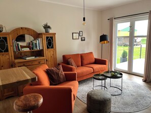 Una sala de estar con sofá, otoman, estantería de madera y una mesa.