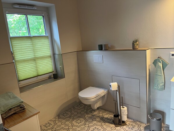 A bathroom with a toilet, a bidet, a towel rack, and a window with blinds. - Gemütliche Fewo für 2 Personen 53qm mit Großer Terrasse (Rubkow)