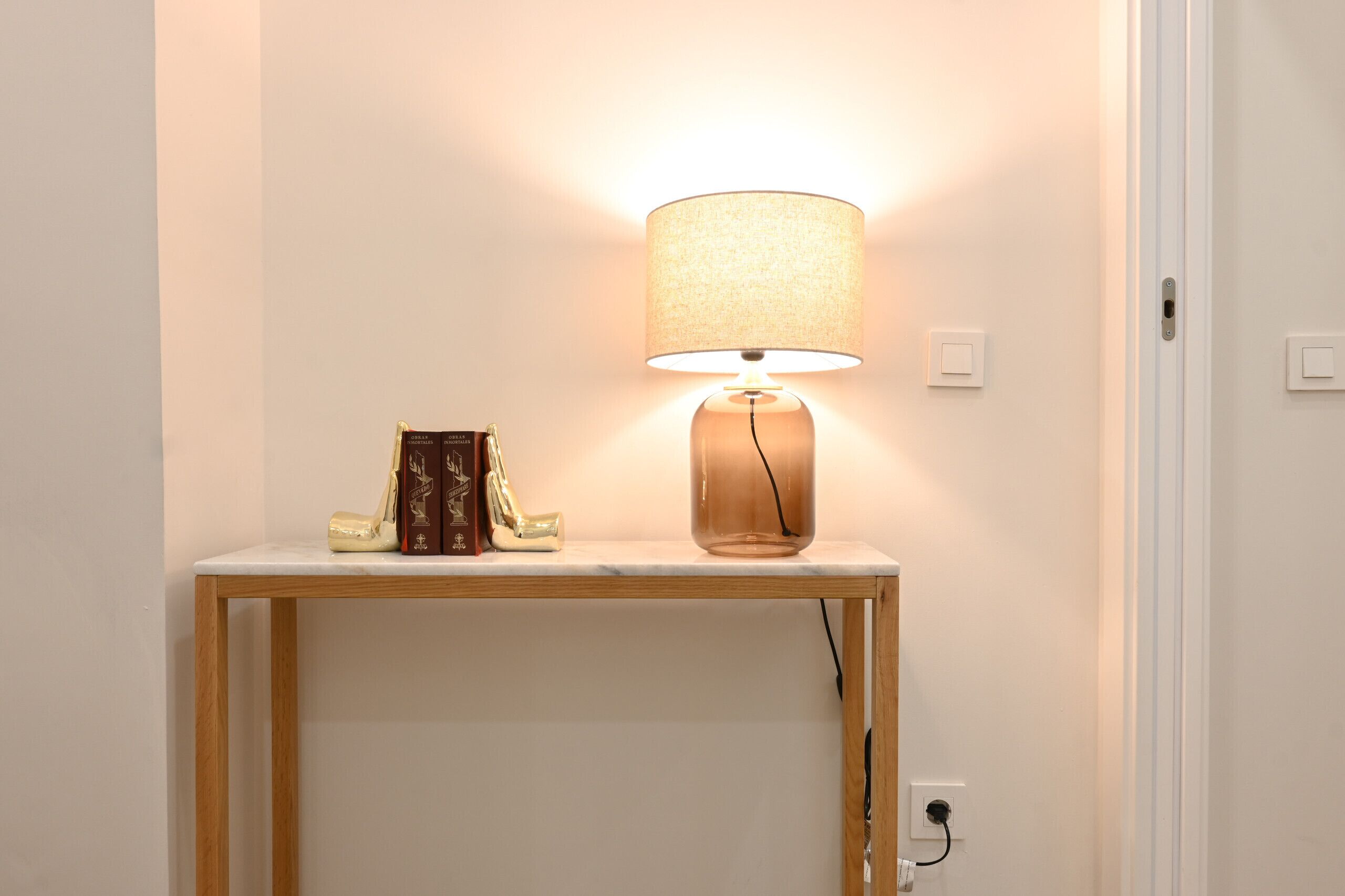 Une table avec une lampe et des livres, placée contre un mur uni.