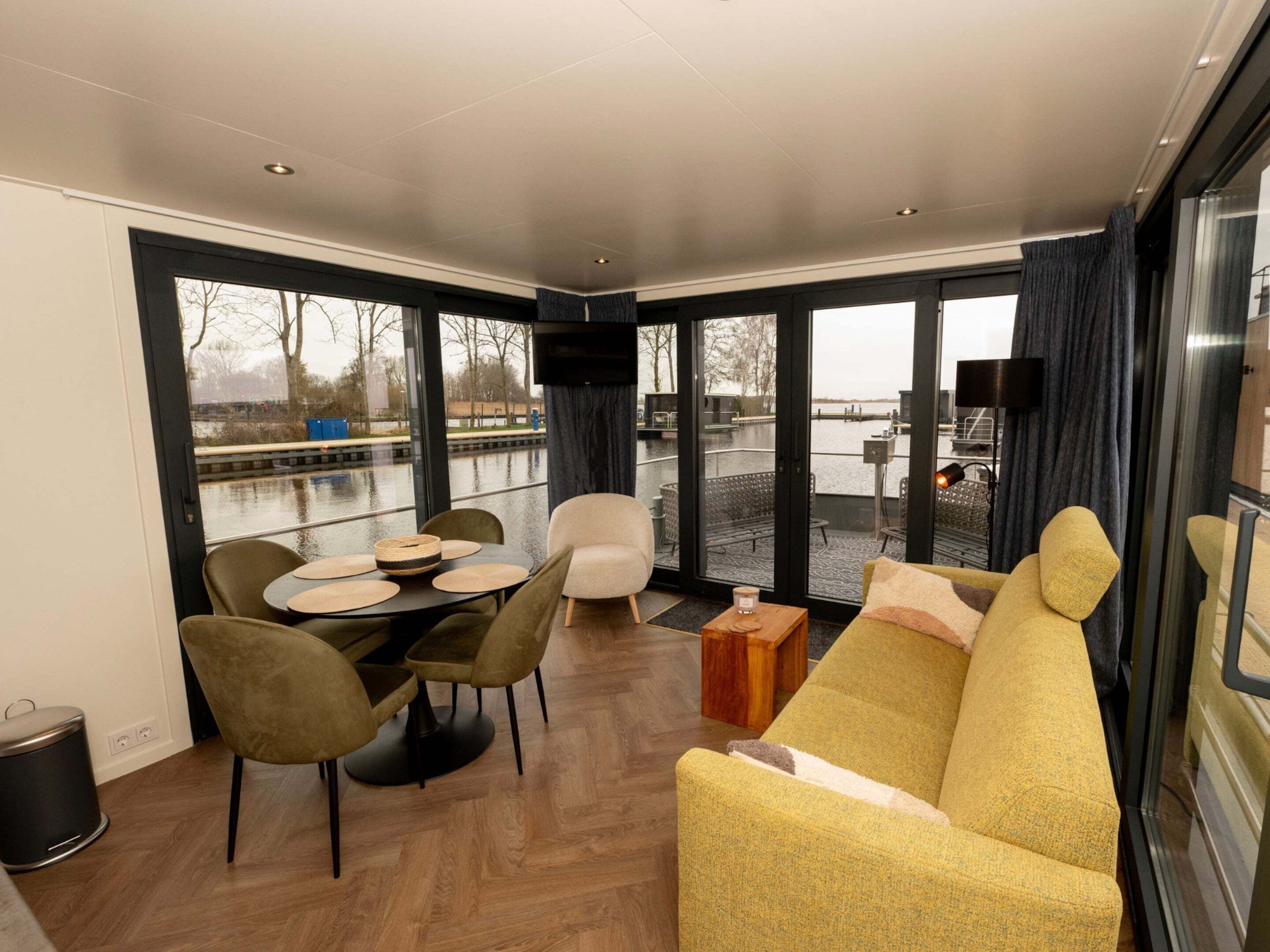 Een modern interieur met een eethoek, bank en grote ramen met uitzicht op een waterpartij.