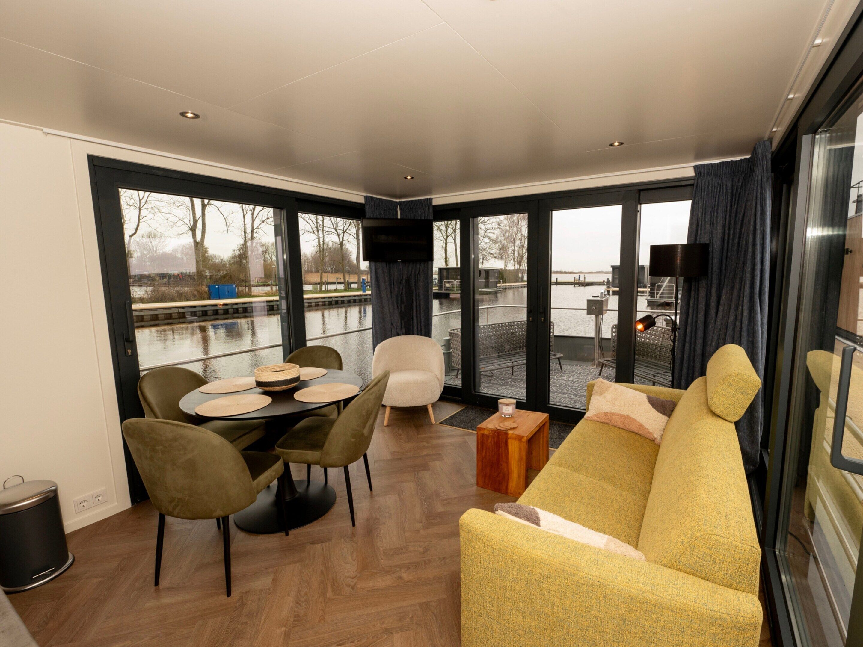A modern interior with a dining area, sofa, and large windows overlooking a body of water.