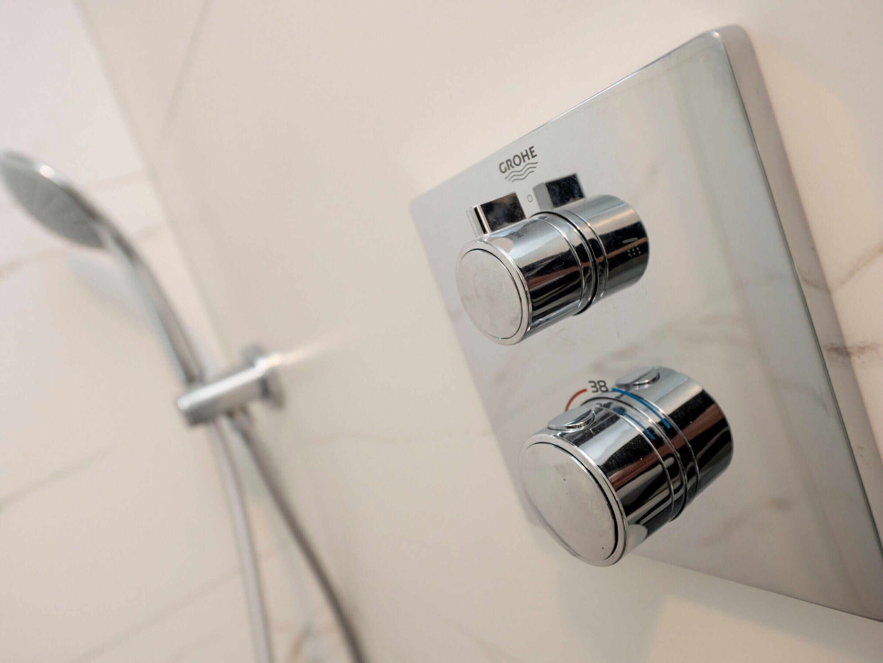 Une salle de bain dotée d’un panneau de commande chromé pour la douche et d’un pommeau de douche à main.