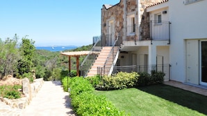 A multi-story building with a stone facade, a staircase leading to a balcony, and a view of the sea. - Holiday Home in Baja Sardinia Near Beaches (Arzachena)