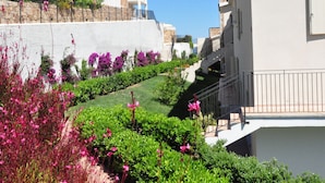 A residential building with a balcony, a garden with pink flowers, and a clear blue sky. - Holiday Home in Baja Sardinia Near Beaches (Arzachena)