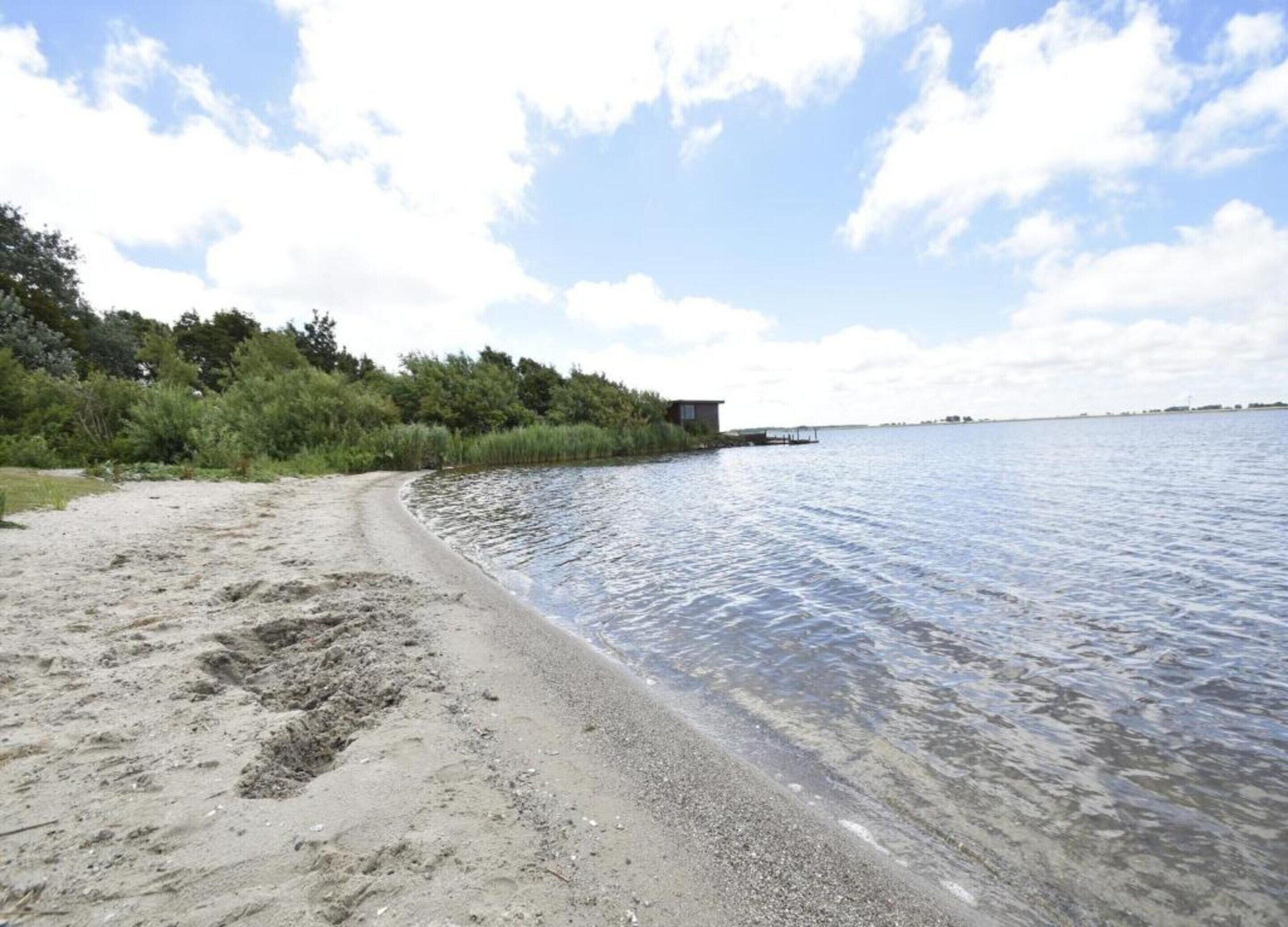 Una playa de arena con agua cristalina, un muelle y follaje en el fondo.