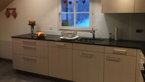 A modern kitchen with a black countertop, beige cabinets, a window with a view of trees, and a small vase with flowers. - Farm in the Agerital (Oberaegeri)