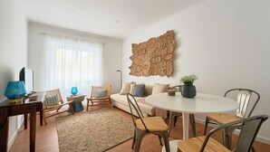 Un salon comprenant un canapé, des fauteuils, une table à manger, un téléviseur et un élément décoratif mural.