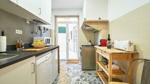 Une cuisine compacte dotée d’un plan de travail noir, de meubles blancs, d’un sol à motifs et d’une table en bois sur laquelle se trouvent un grille-pain et un verre à vin.