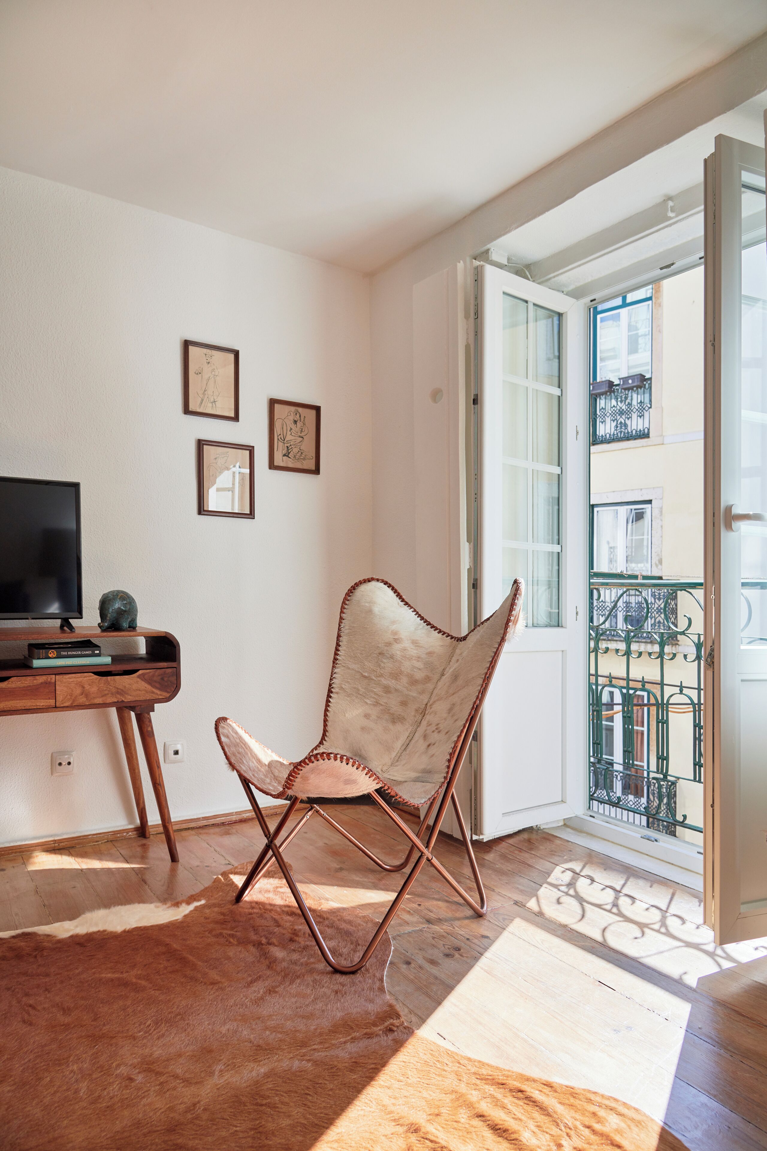 Une pièce comprenant un bureau en bois, un téléviseur, un fauteuil rembourré et donnant sur un balcon avec une balustrade.