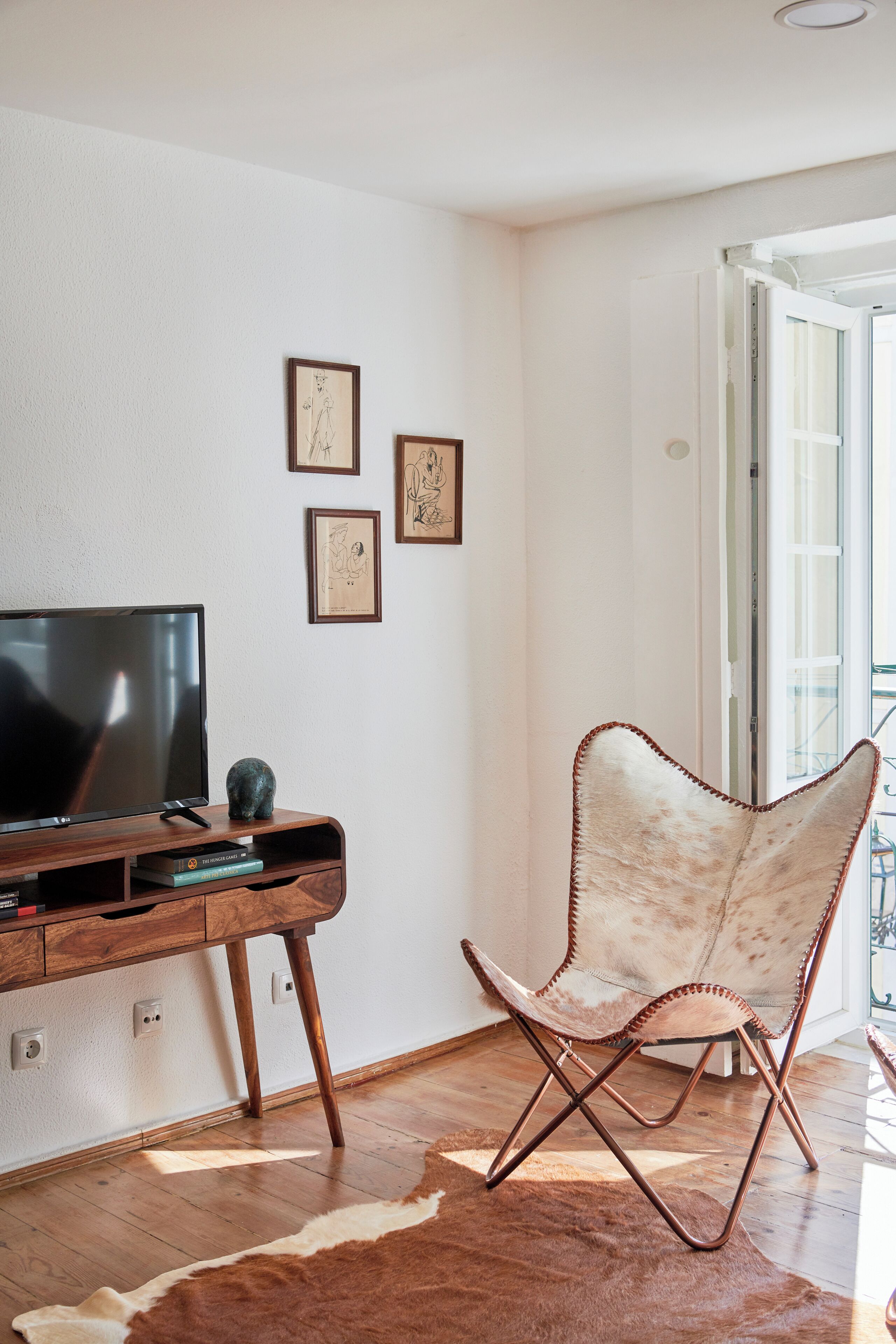 A room with a flat-screen TV on a wooden stand, a cowhide rug, a unique chair, and framed artwork on the wall.