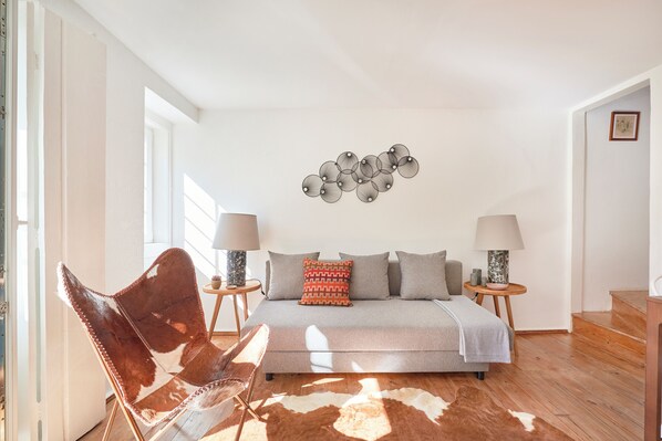 A bedroom with a bed, two bedside tables, a chair, a wall art piece, and a wooden floor.