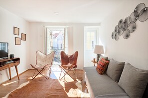 A living room with a sofa, a leather chair, a flat-screen TV, a wooden desk, and a cowhide rug.