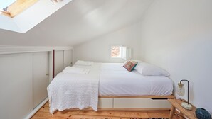 A bedroom with a skylight, a bed with white bedding, a bedside table with a lamp, and a wooden floor. - Central, Comfy And Light-Filled Apt, By Timecooler (Lisbon)