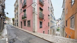 A narrow street with buildings on either side, including a pink building with balconies and a sign. - Central, Comfy And Light-Filled Apt, By Timecooler (Lisbon)