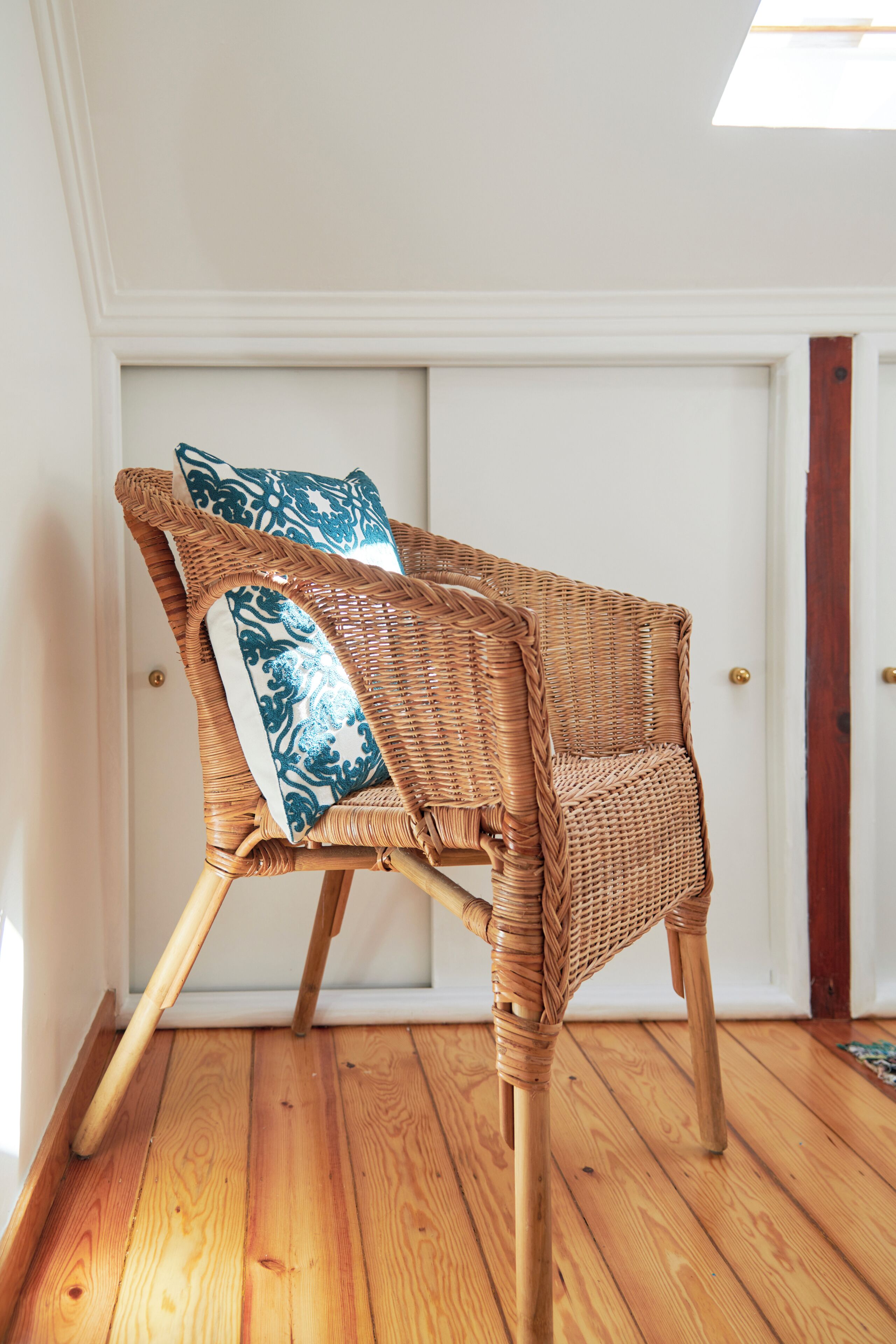 A wicker chair with a patterned cushion in a room with wooden flooring and white walls.