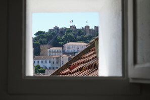 A view through a window of a building with a castle-like structure on a hill, a flag, and a tiled roof. - Central, Comfy And Light-Filled Apt, By Timecooler (Lisbon)