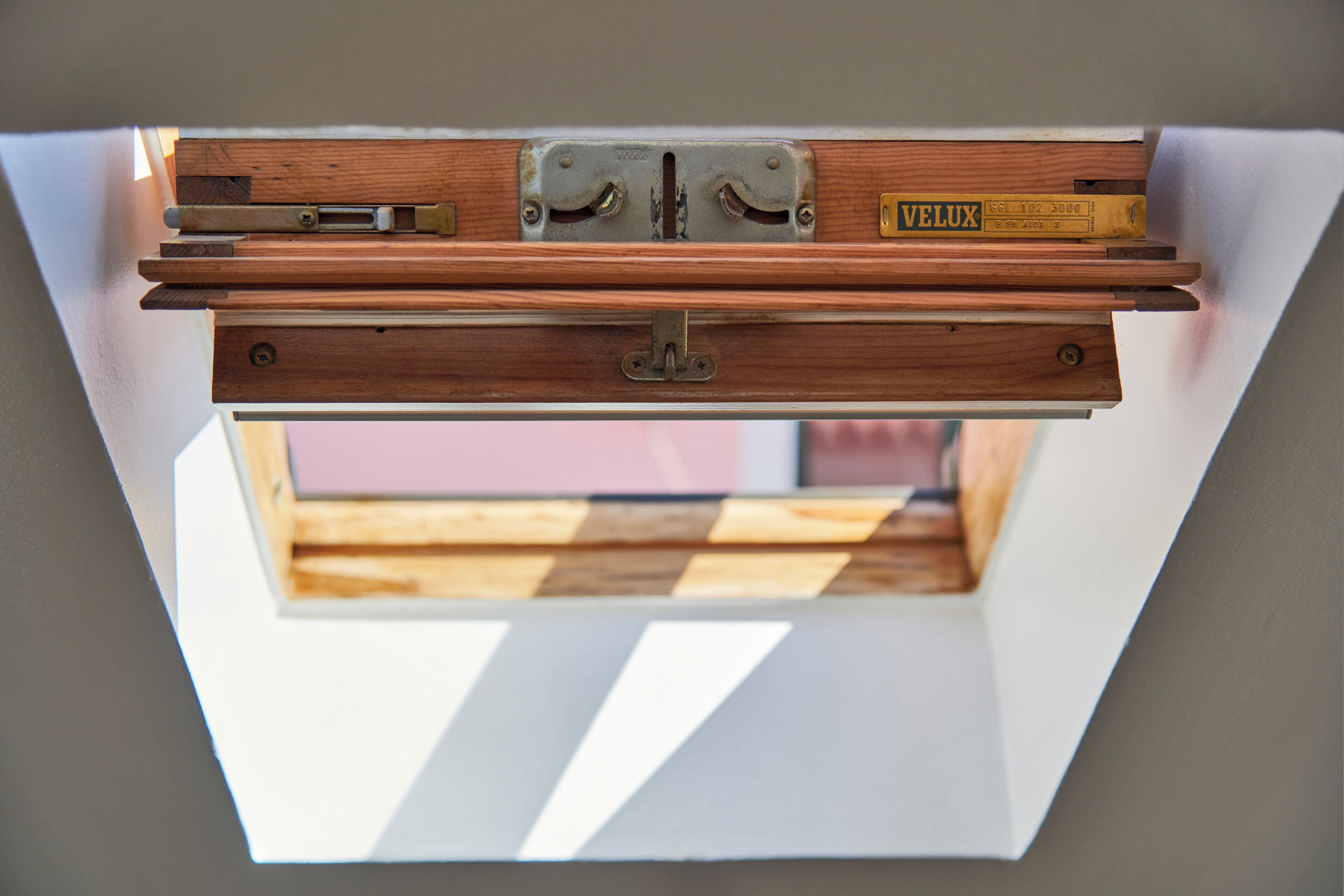 A skylight with a wooden frame and metal hinges, a Velux brand label, and a view of a wooden structure outside.