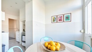A modern kitchen with white cabinets, a dining table with a basket of lemons, and a blue chair. - Charming And Central Br Apartments, By Timecooler (Lisbon)