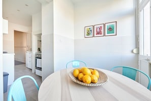 A modern kitchen with white cabinets, a dining table with a basket of lemons, and a blue chair.