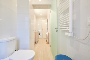 A narrow bathroom with a toilet, a washing machine, and a towel rack.