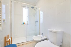 A modern bathroom with a glass-enclosed shower, a bidet, and a toilet.