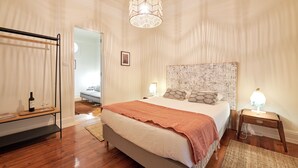 A bedroom with a bed, bedside lamps, a hanging light fixture, a wooden floor, and a door leading to another room. - Charming And Central Br Apartments, By Timecooler (Lisbon)