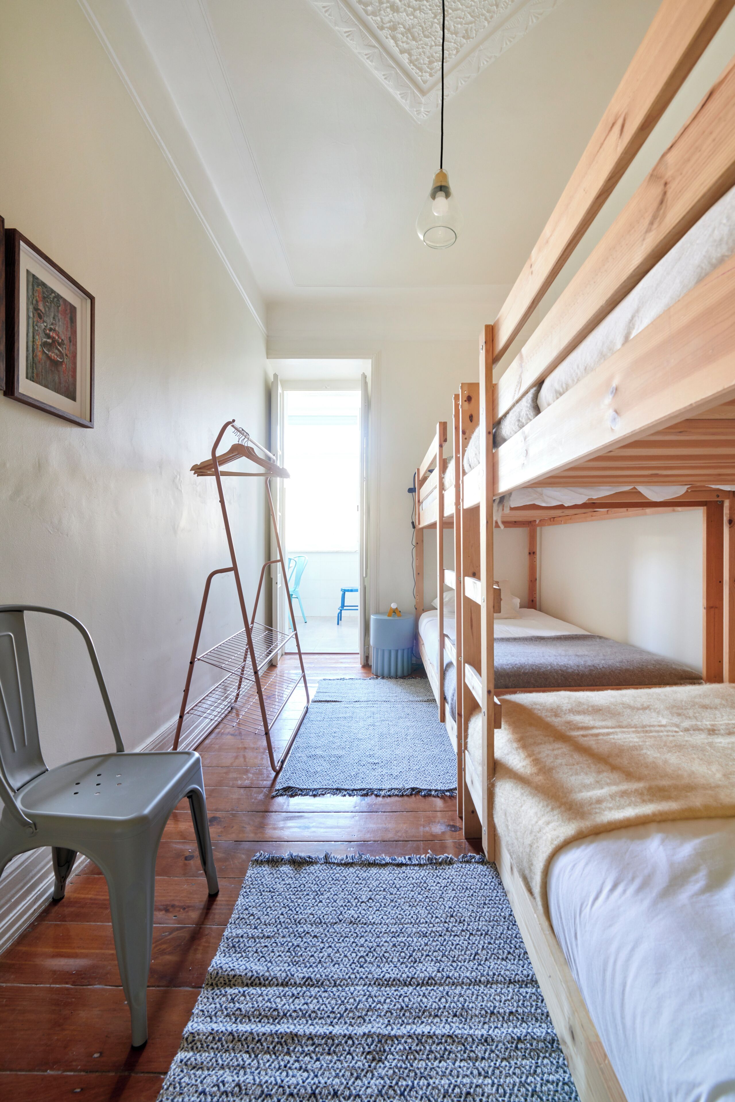 Een kamer met stapelbedden, een stoel, een kledingroede en een deur naar een andere kamer.