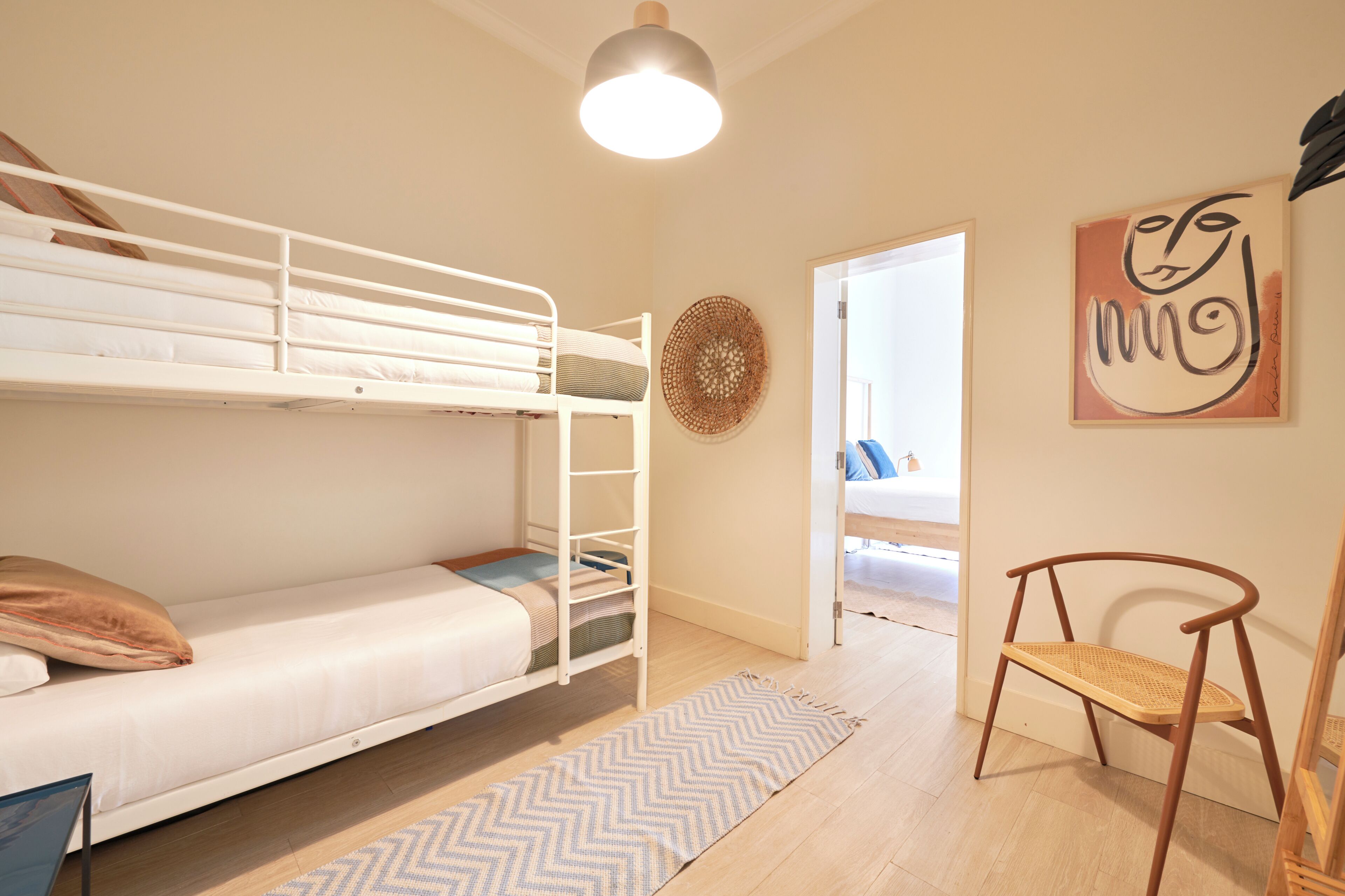A bunk bed room with a herringbone-patterned rug, a woven wall decoration, and a wooden chair.