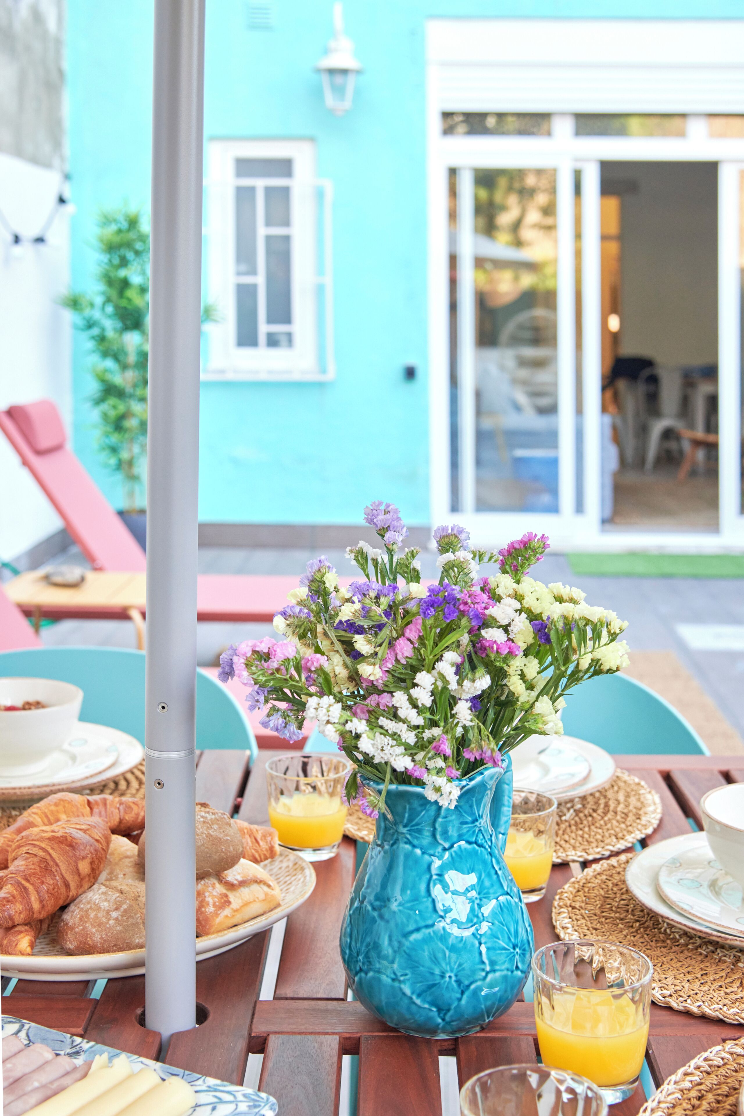 A table set with breakfast items, a vase of flowers, and a view of a blue building.