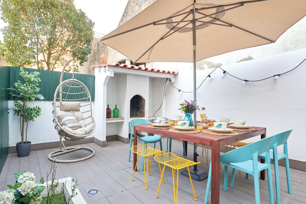 A patio with a wooden table, chairs, a hanging chair, and a large umbrella.