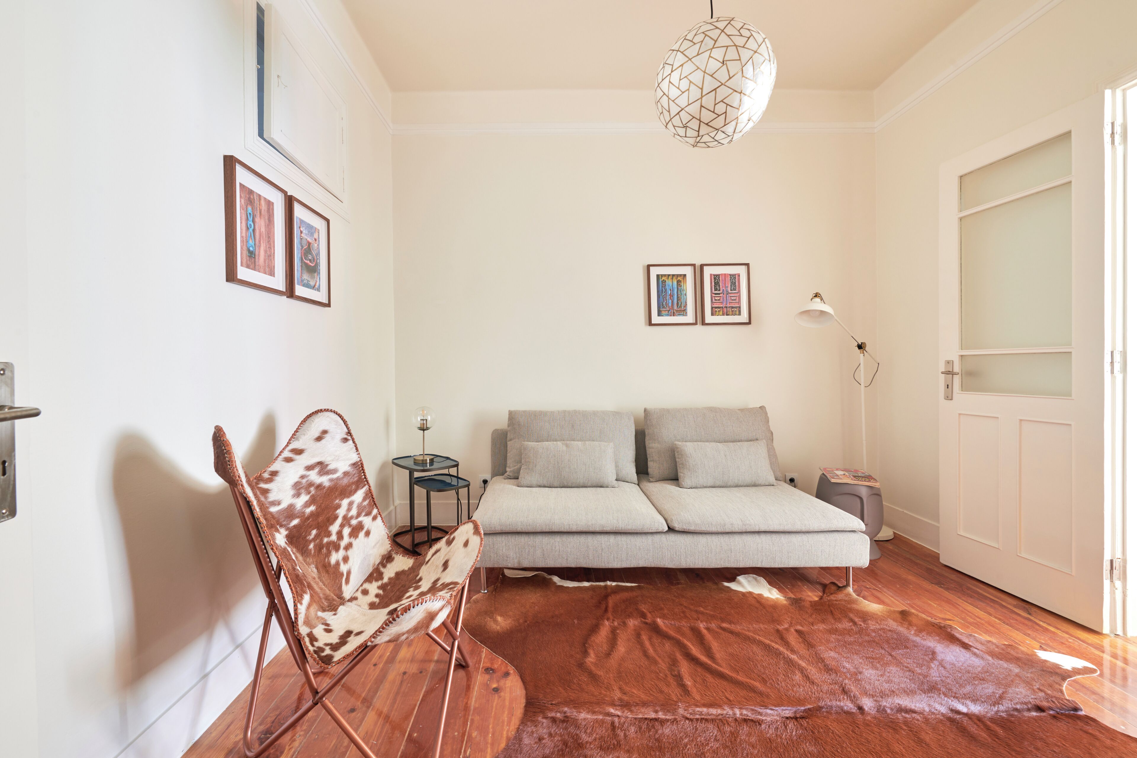 A room with a sofa, a cowhide rug, a chair, a lamp, and framed pictures on the wall.